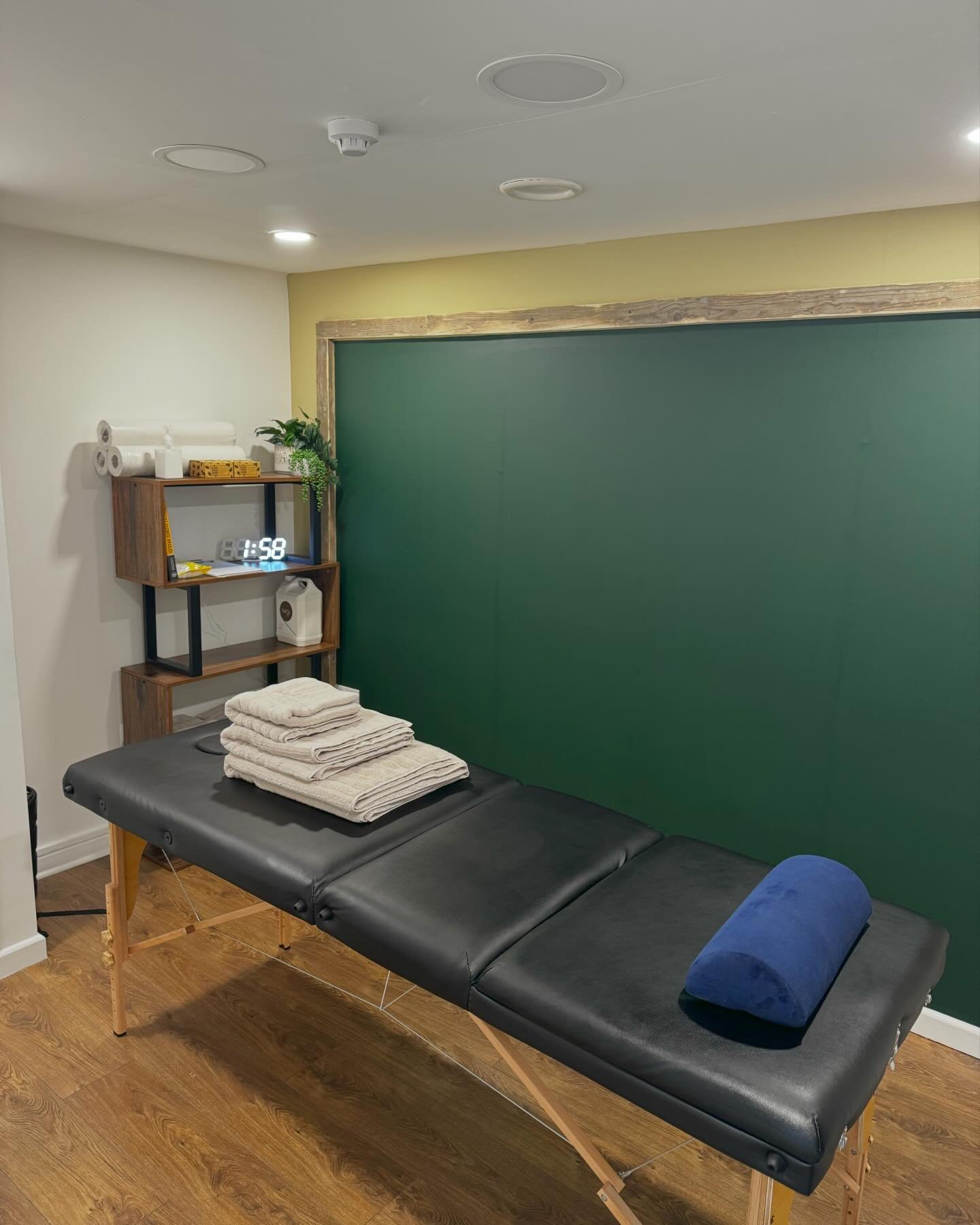 Treatment room with massage couch, towels and green feature wall